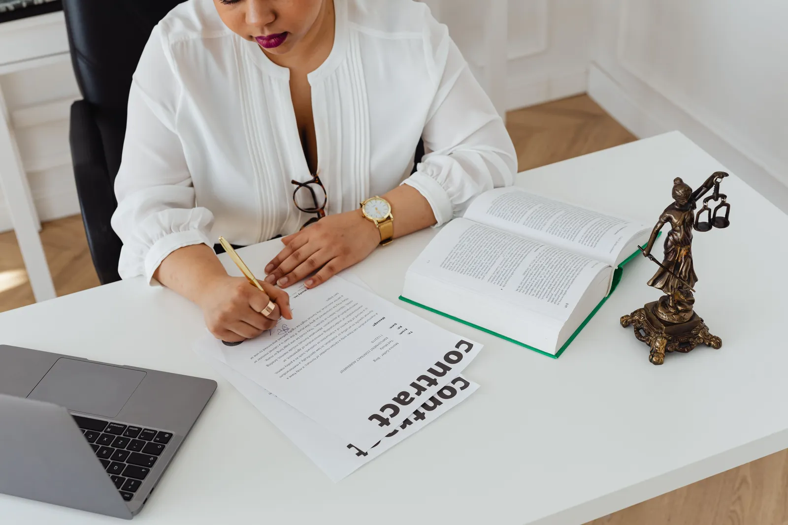 Advogada escrevendo sobre contratos em uma mesa com livros de direito e um notebook aberto