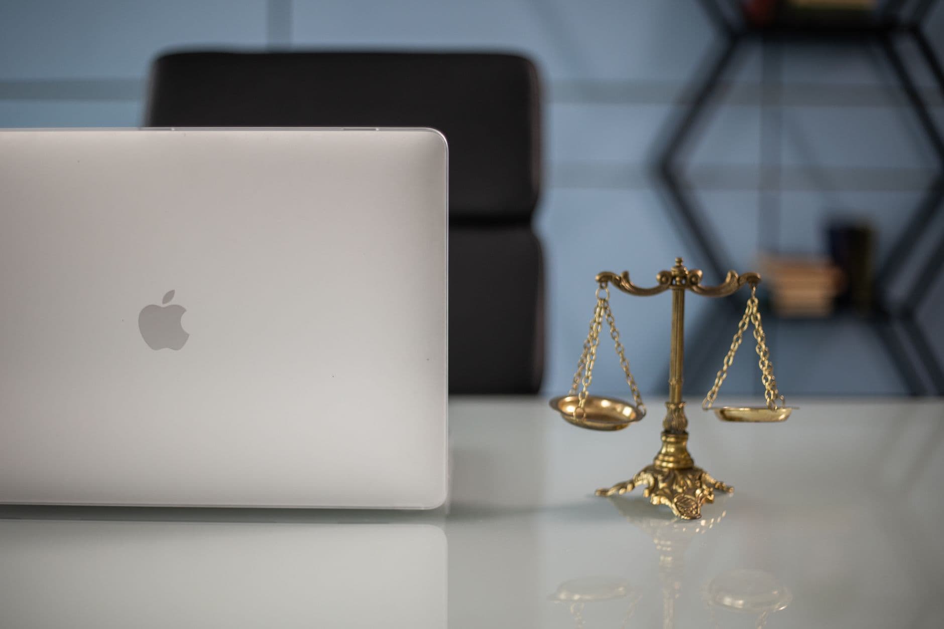 Notebook ao lado de uma balança da justiça sobre a mesa de um escritório de advocacia